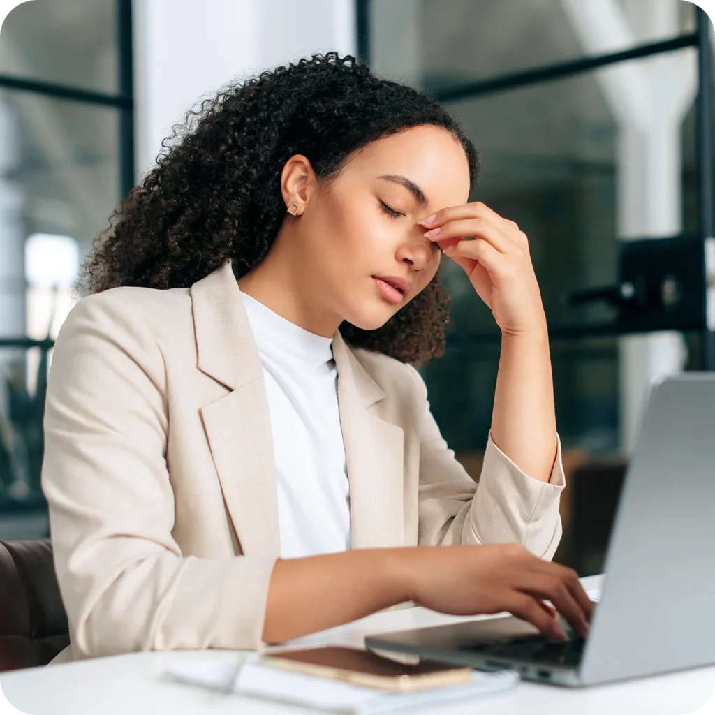 Woman working on a laptop in a modern office, appearing stressed or overwhelmed while managing business tasks.